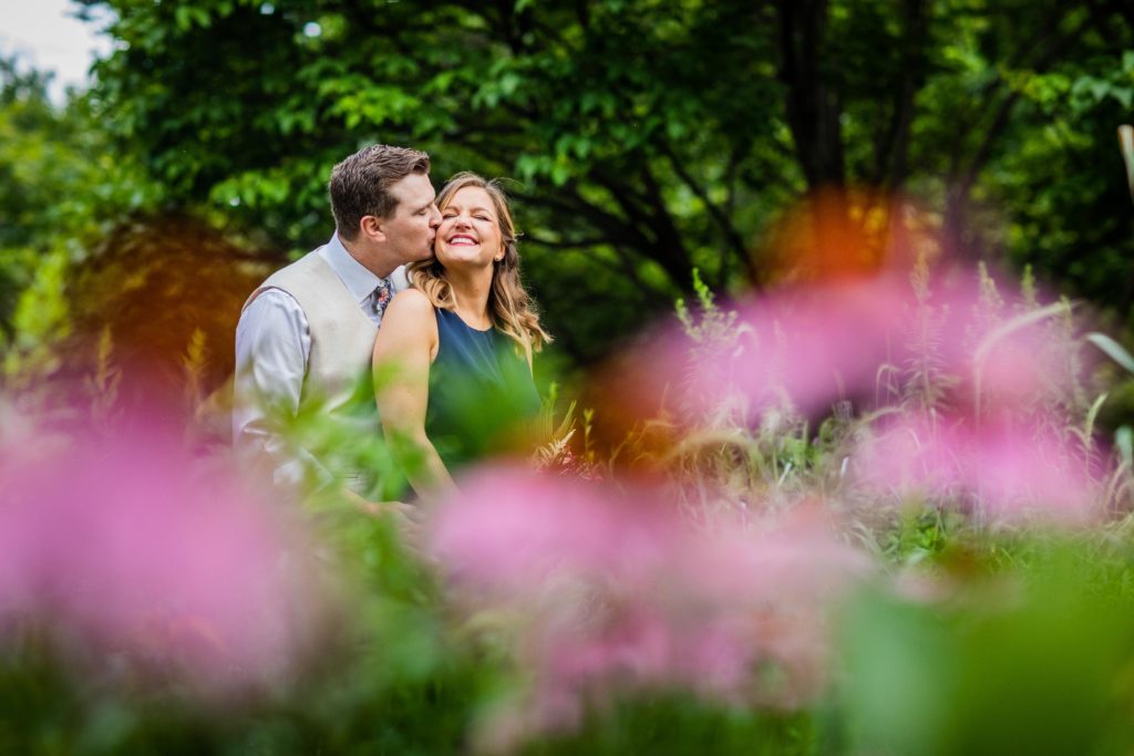 Groom kissing the bride on the cheek in Welles Park behind flowers