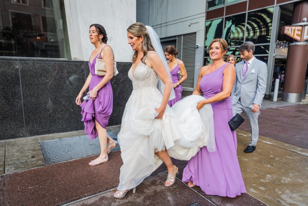 Maid of honor holding bride's dress as they walk down the street