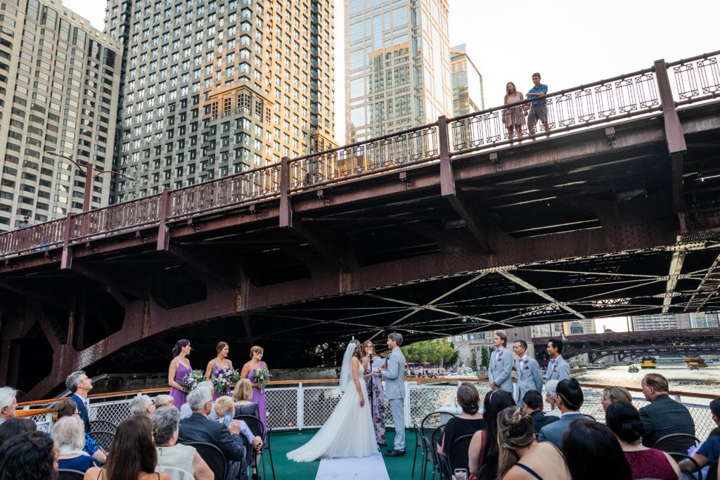 Bride and groom being married while people watch from a bridge