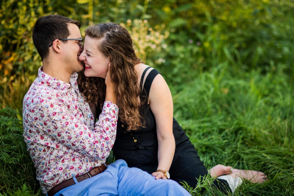 Man pulling in woman for a kiss while sitting in the grass during their south pond engagement session