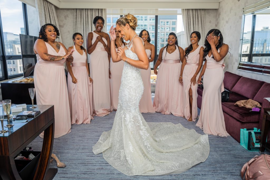 Bride showing off her dress to her bridesmaids before her wedding at Venue SIX10