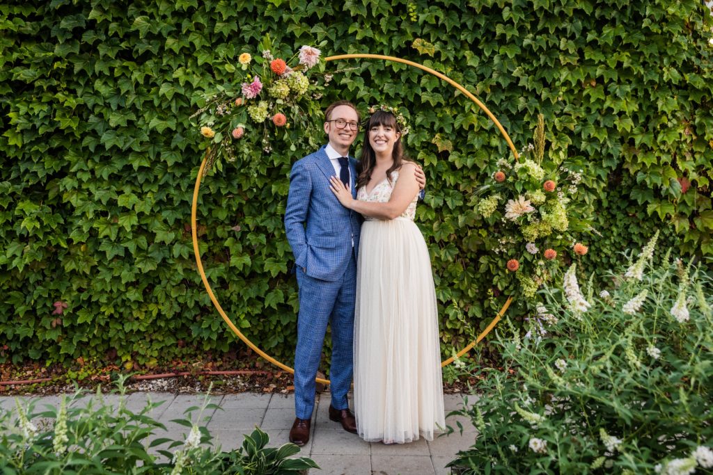 Couple posing under their floral arch at their Big Delicious Planet Wedding