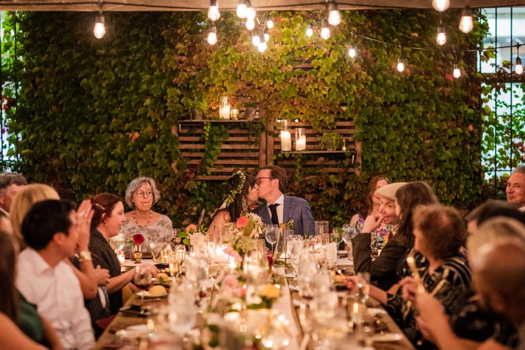 Bride and groom kissing at the dinner table during their Big Delicious Planet Wedding reception
