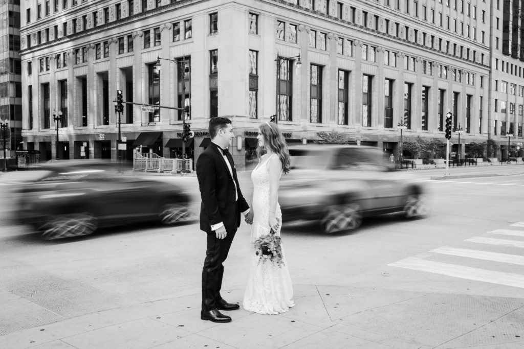Bride and groom posing on a street corner while cars whiz by in the background