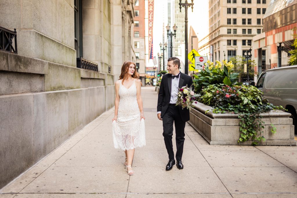 Bride holding her dress while walking with the groom, who's holding the flowers