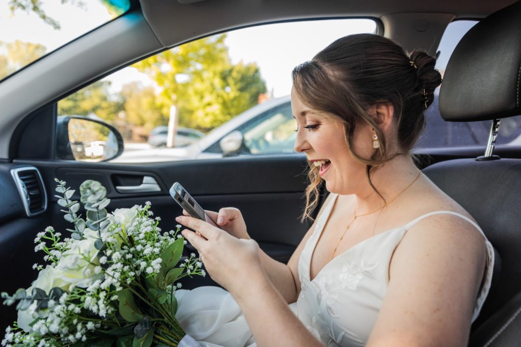 Bride looking at her phone in the car while smiling