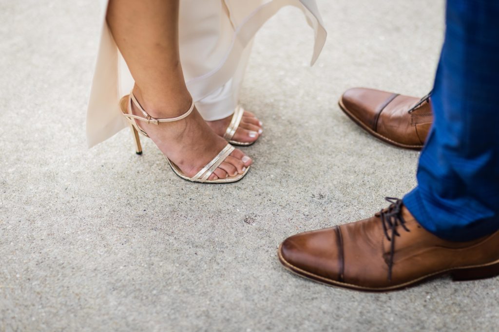close up of bride's heels next to the grooms shoes