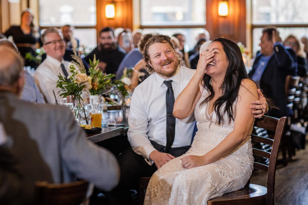 Bride covers her face and laughs while listening to a speech