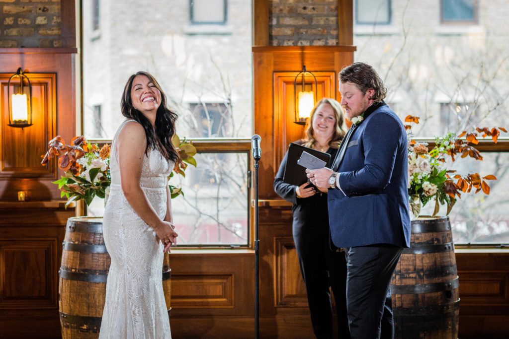 Bride laughs at the altar while listening to the groom read his vows at their Revolution Brewing Wedding