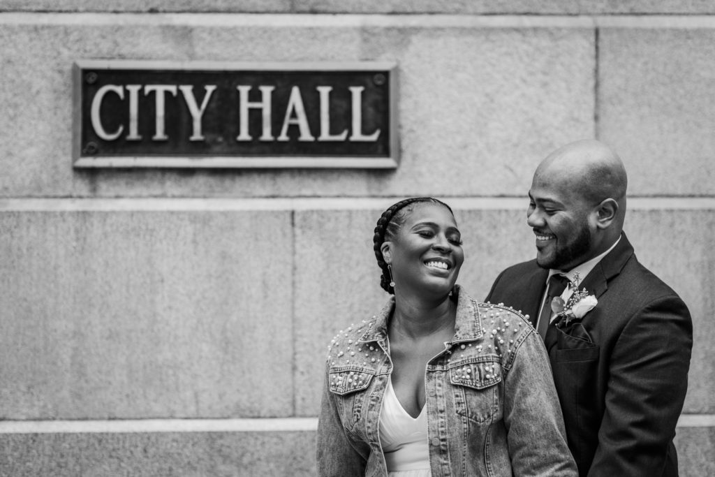 Bride and groom laugh on Randolph street in from of the City Hall sign in Chicago
