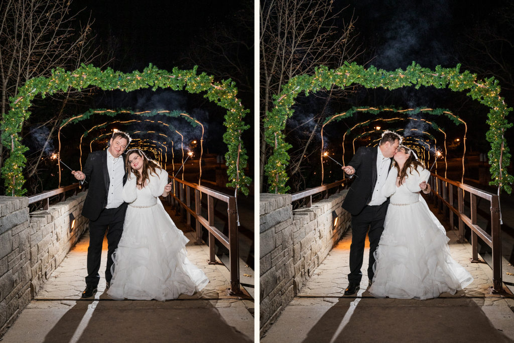 Bride and groom hold sparklers and kiss under a canopy of pine tree branches
