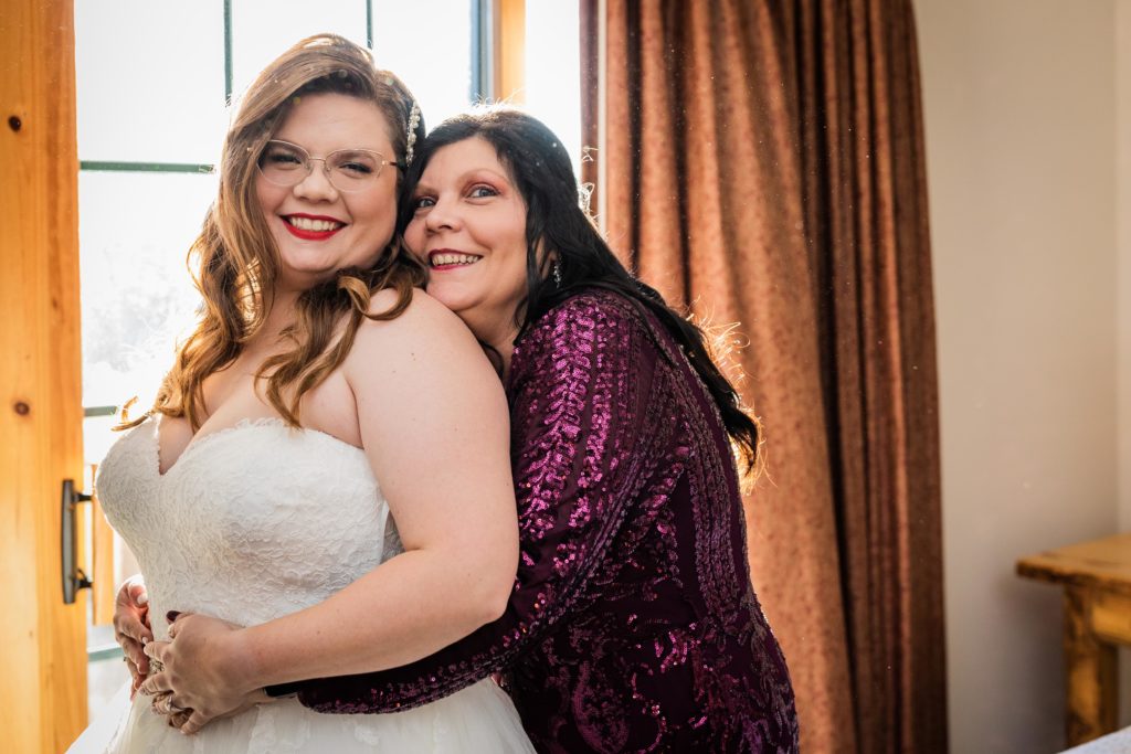 Mom and her daughter, the bride, smile after the dress is put on