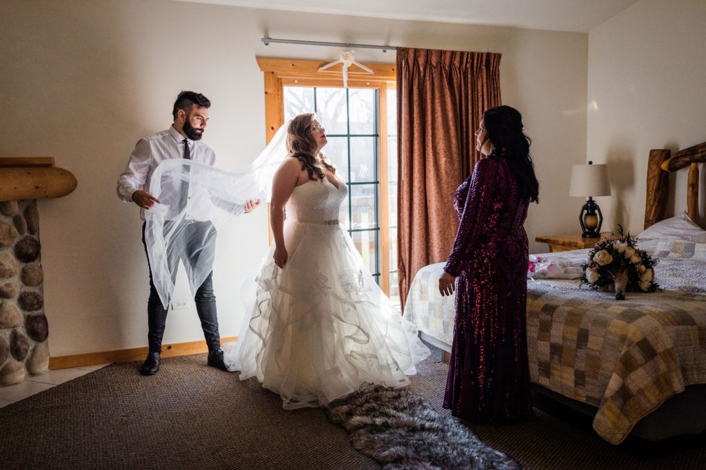 Bride stands in front of a window while her friend adjusts her veil before her wedding at  Starved Rock