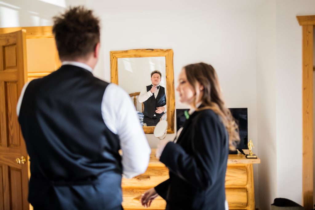 Groom looks at his reflection in the mirror as he adjusts his tie