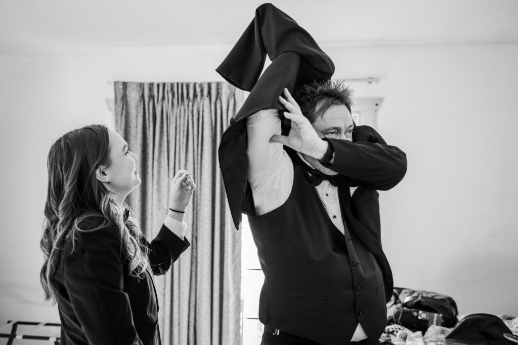Daughter laughs as her father, the groom, puts on his suit jacket
