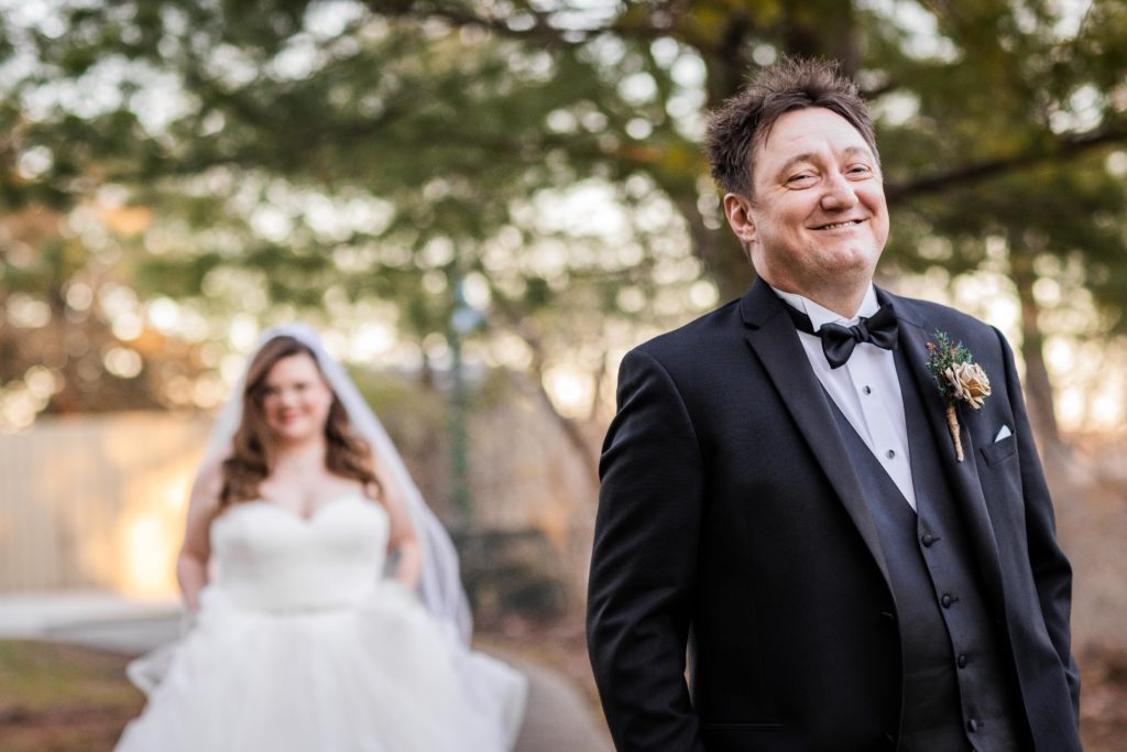 Groom smiles as his bride approaches him from behind before their wedding at Starved Rock