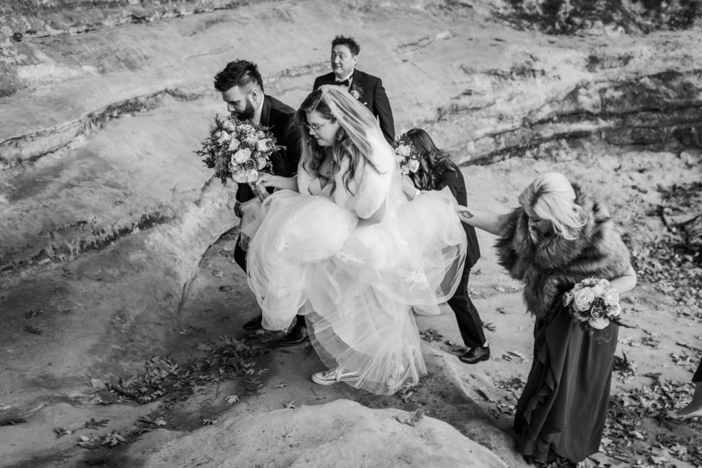 Wedding party walks up rock face while holding bride's dress