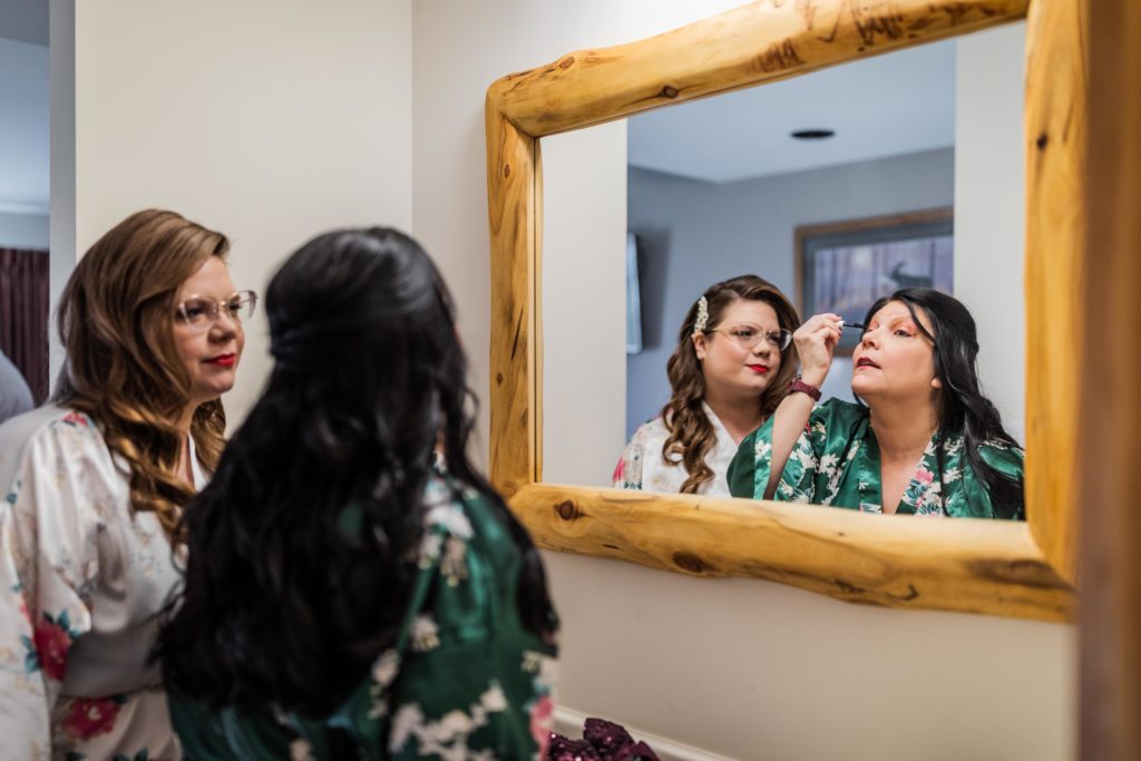 Bride watches her mom put on makeup in the mirror