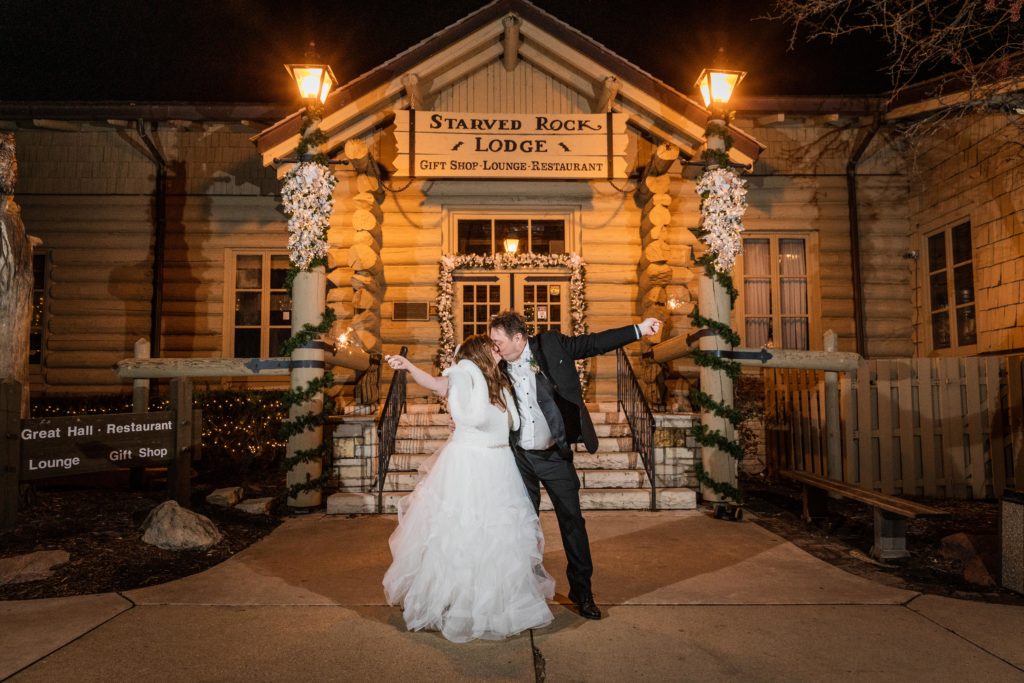 Bride and groom kiss while holding sparklers in front of the Starved Rock Lodge