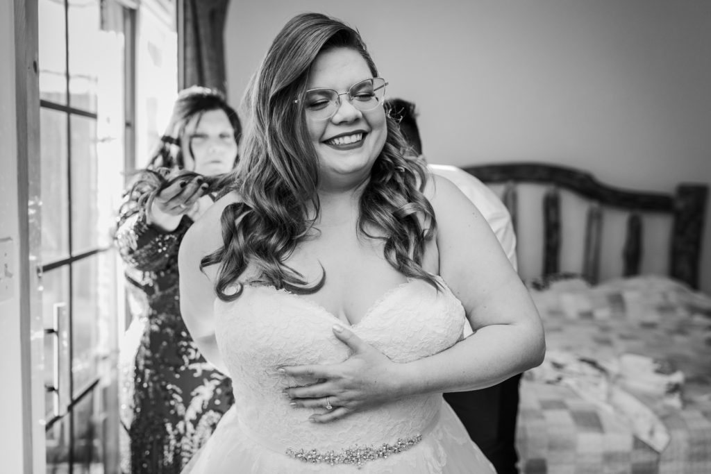 Bride laughs as her mom and friend help put her dress on