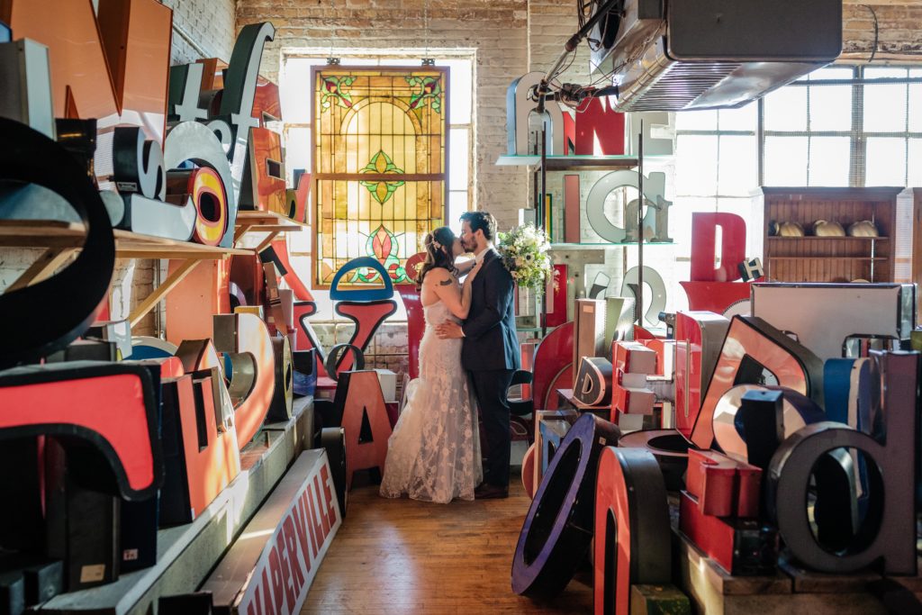 Bride and groom kiss while surrounded by antique furniture