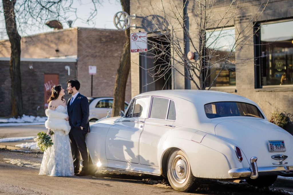 Bride and groom pose with vintage car outside of Ovation Chicago