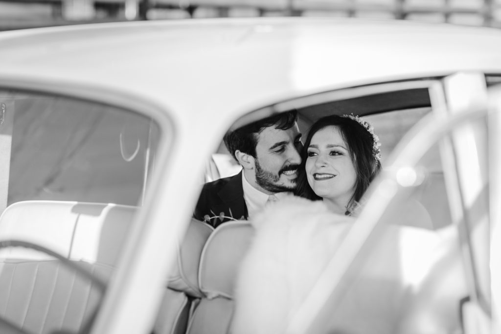 Groom looks at bride while she smiles in a vintage car outside of Ovation Chicago