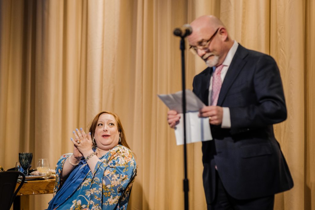 Mother of the groom claps while watching her husband speak at Ovation Chicago