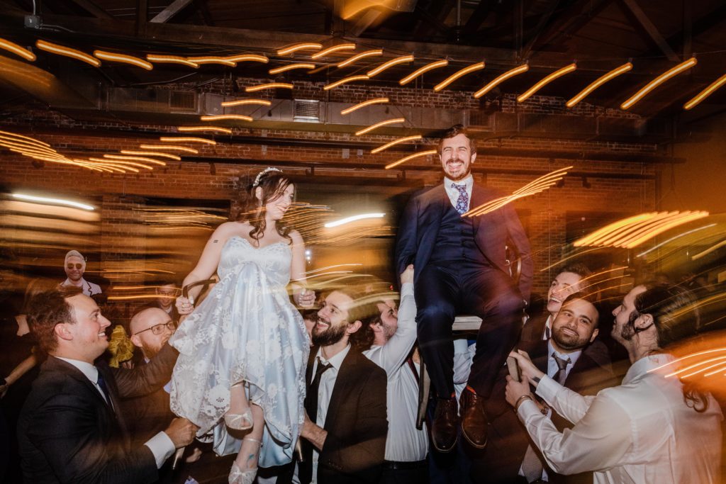 Couple laugh as they get picked up in chairs for the hora at Ovation Chicago