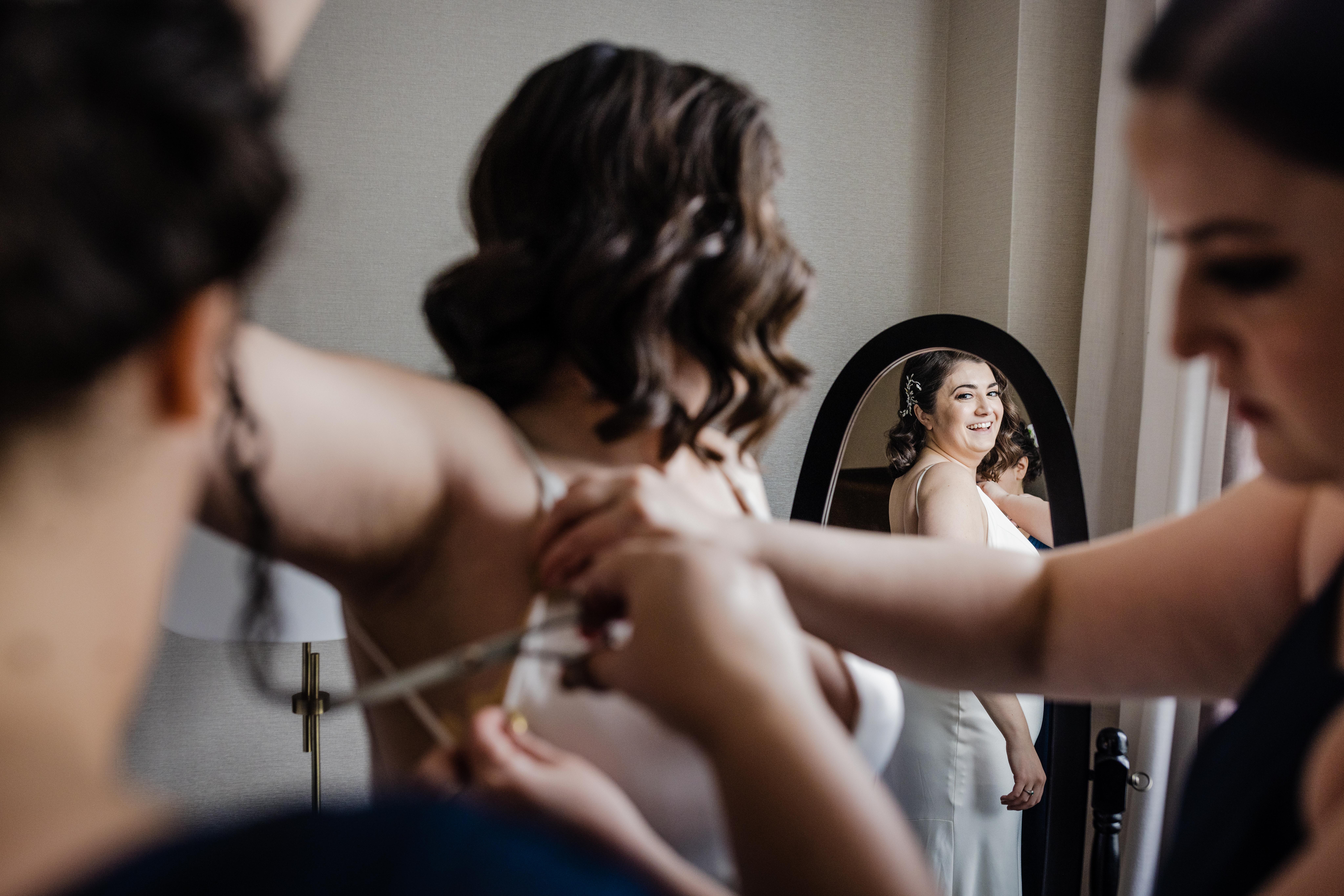 Bride looking at herself in the mirror with bridesmaids at the Clardige Hotel