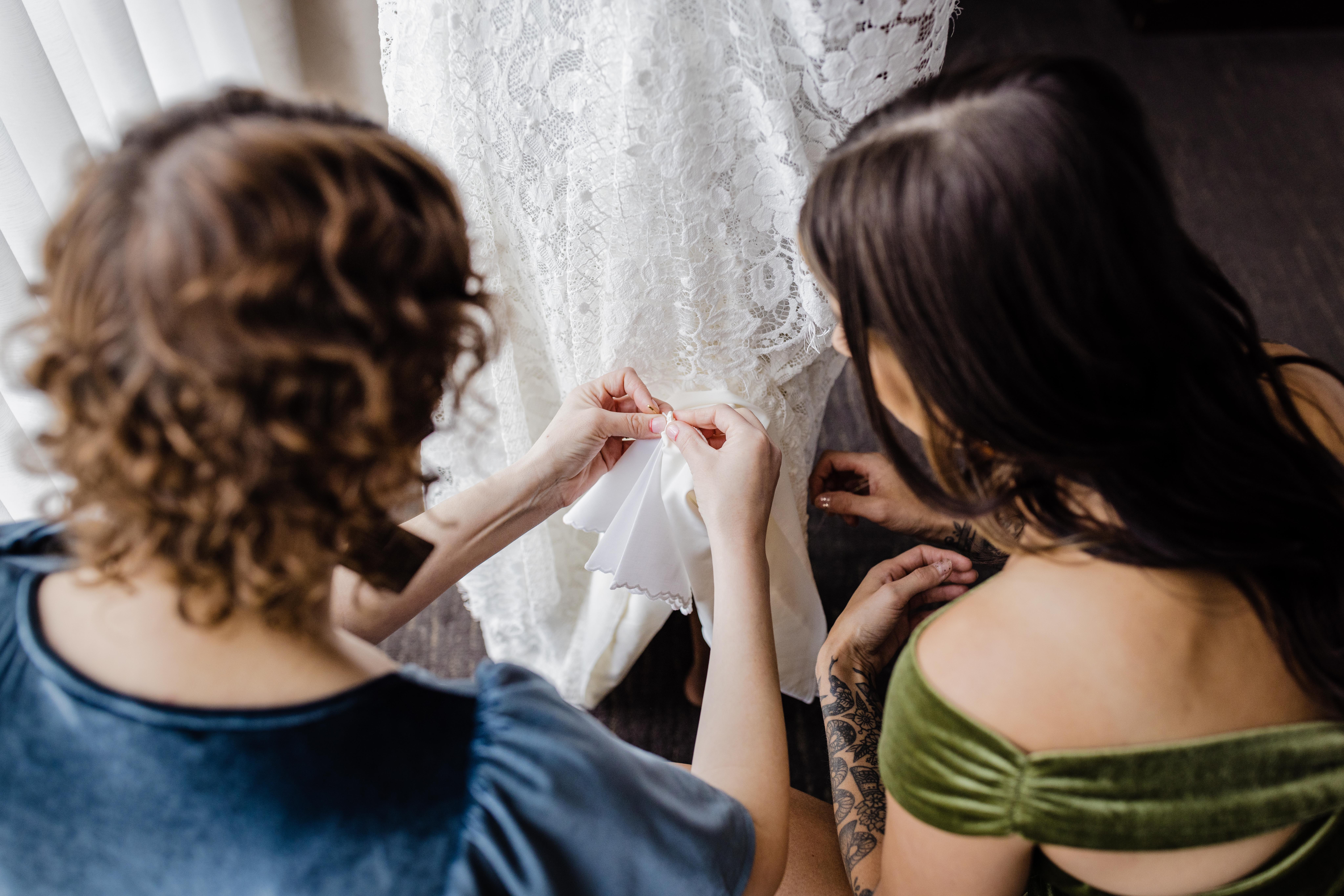 Bridesmaids sewing in something old into the bride's dress